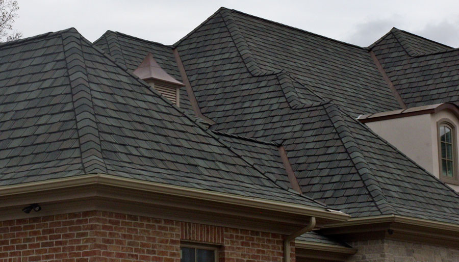 This is an image of just the top of a beautiful new blackish/grayish roof that our South Shore roofing company installed. The roof has many peaks and levels and was installed on a beautiful brick home. It is an example of the roof repair, roof replacement, and roof installation work that our South Shore roofing contractors' business does for homes and businesses in Braintree, Duxbury, Marshfield, Pembroke, Quincy, Hanover, Norwell, Plymouth, Weymouth, Scituate, and Cohasset MA