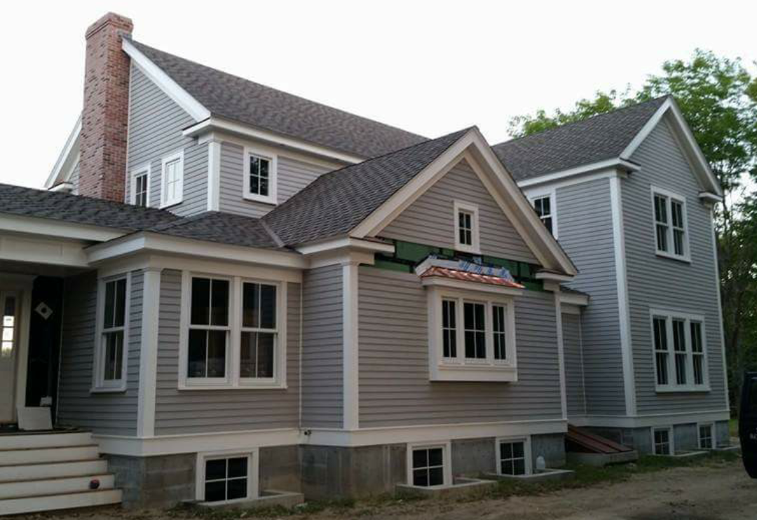 This is the image of a gray home with white door and window trim with numerous roof peaks with a black shingles adorning the roof. The house is one of many homes in the South Shore towns of Duxbury, Marshfield, Pembroke, Quincy, Hanover, Norwell, Plymouth, Weymouth, Cohasset, and Scituate that our South Shore roofing contractors' business has done roof repair, roof replacement, roof installation, etc. work on.