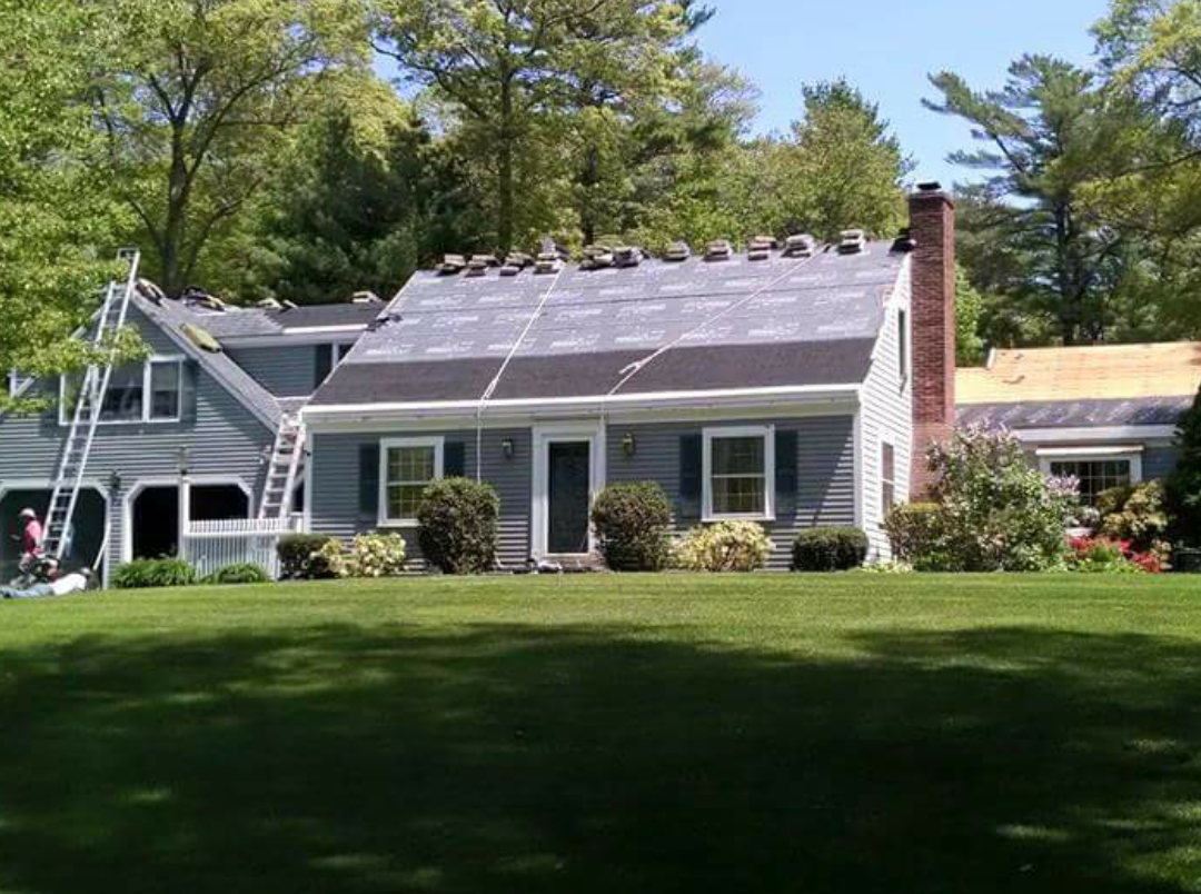 This is the image of a gray home with white door and window trim with numerous roof peaks and black shutters. Part of the roof is missing and there are ladders leaning up on the house indicating that roof work is being done. The house is one of many homes in the South Shore towns of Duxbury, Marshfield, Pembroke, Quincy, Hanover, Norwell, Plymouth, Weymouth, Cohasset, and Scituate that our South Shore roofing contractors' business has done roof repair, roof replacement, roof installation, etc. work on.