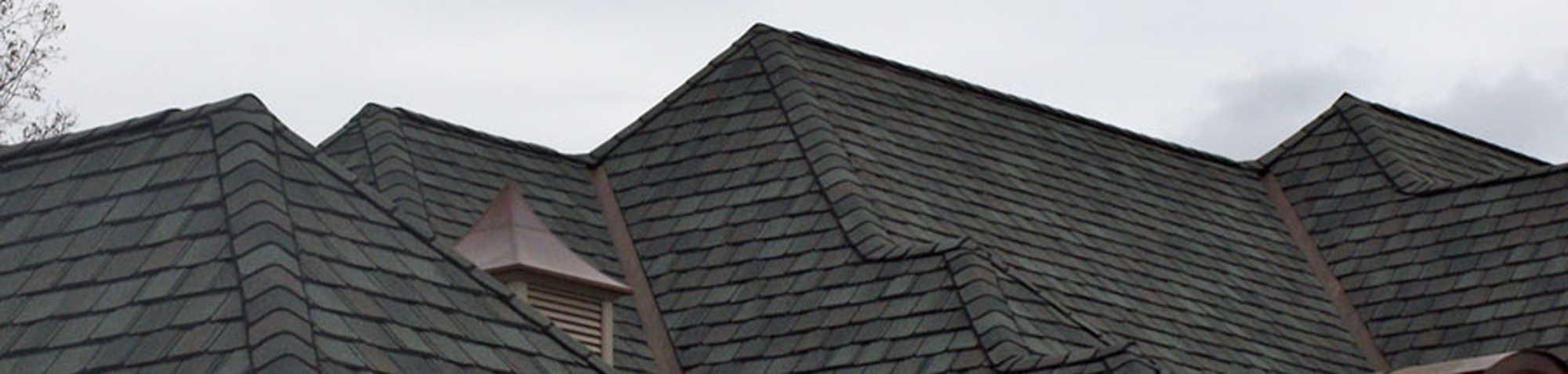 This is an image of just the top of a beautiful new blackish/grayish roof that our South Shore roofing company installed on a home that has multiple roof peaks . The roof has many peaks and levels and was installed on a beautiful brick home. It is an example of the roof repair, roof replacement, and roof installation work that our South Shore roofing contractors' business does for homes and businesses in Braintree, Duxbury, Marshfield, Pembroke, Quincy, Hanover, Norwell, Plymouth, Weymouth, Scituate, and Cohasset MA