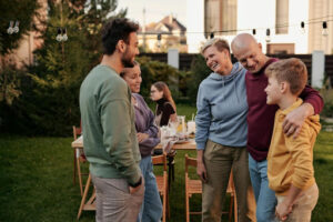 This image shows an ethnically and age diverse group of individuals outside at get-together. It includes a string of lights and you can see city buildings in the background.