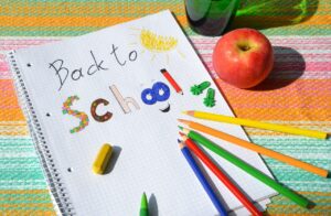 this is an image of a piece of paper lying on top of something patterned like a tablecloth or placemat that says "back to school" on it and the paper has an apple sitting to the right of it.